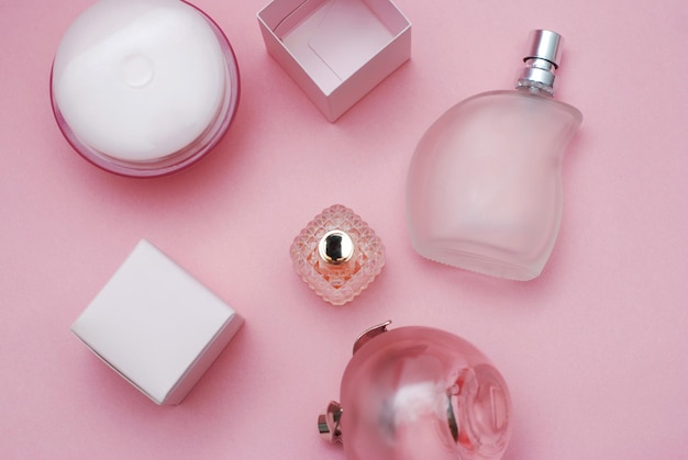 Botellas de Perfumes de Mujer y Cosméticos en Hermosa Botella de Vidrio y sobre fondo de color rosa. Concepto de moda y belleza.