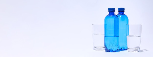 Botellas de plástico azul y vasos de agua sobre fondo claro