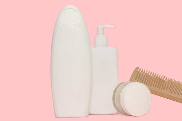 Botellas de plástico blancas para productos cosméticos peine de madera sobre un fondo rosado