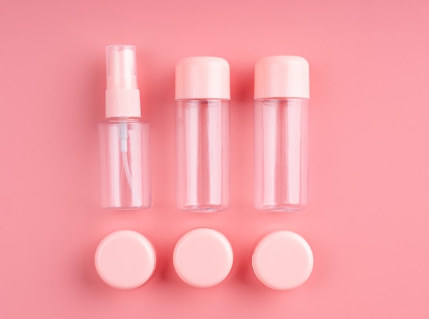 Botellas de plástico vacías y tubos para cosméticos en la vista superior de fondo rosa pastel plano