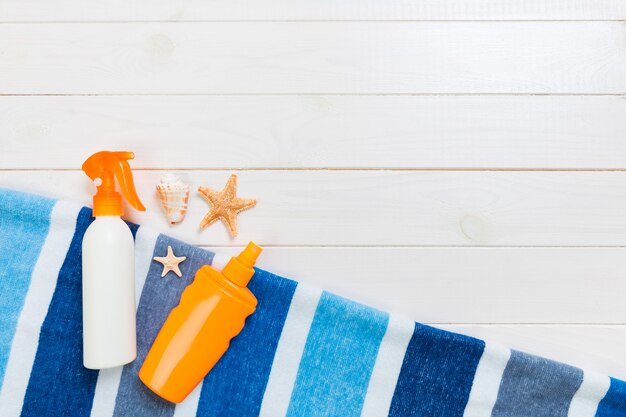 Botellas de protector solar con estrella de mar y toalla azul sobre mesa de madera blanca con espacio de copia. Vista superior de accesorios de salud de viaje.