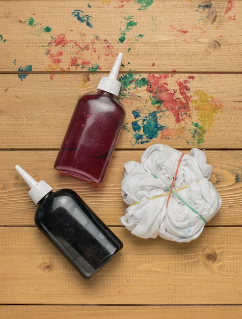 Botellas de tintes rojos y negros para teñir ropa y una camiseta blanca enrollada sobre una mesa de madera Lay Flat