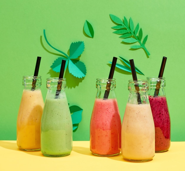 Foto botellas de varios batidos de plátano y bayas de colores sobre fondo de hoja de papel verde