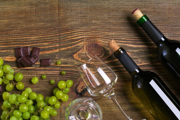 Botellas y vasos de vino chocolate y uvas maduras sobre fondo de madera