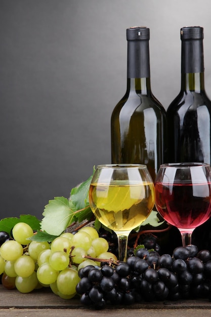 Botellas y vasos de vino y uvas sobre fondo gris