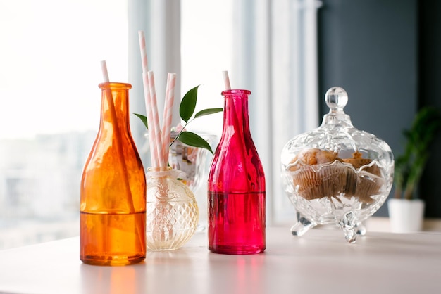 Botellas de vidrio de colores brillantes con pajitas de papel para bebidas o cócteles y un tazón de galletas