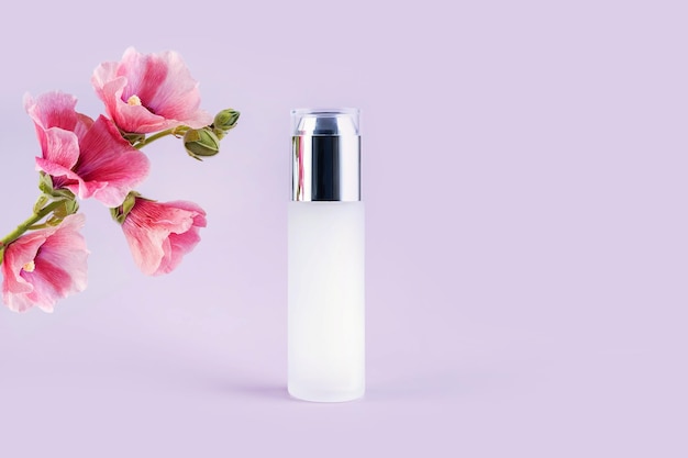 Botellas de vidrio para cosméticos y flores sobre un fondo morado.