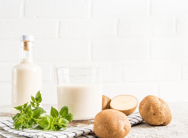 Botellas de vidrio de leche vegetal de patata alternativa contra una pared de ladrillo blanco el concepto de una dieta vegetariana saludable