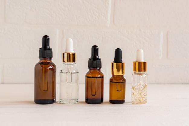 Botellas de vidrio oscuro y cosmético transparente con suero facial o aceite esencial sobre un fondo de madera. Productos cosméticos de belleza sin marca.