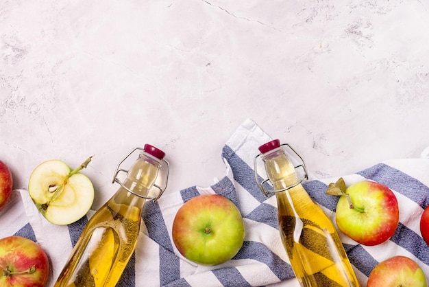 Botellas de vinagre de manzana y manzanas maduras en una toalla de cocina Fondo gris claro Cosecha Otoño