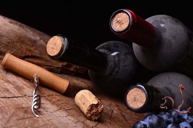 Botellas de vino, corcho y uva sobre superficie de madera