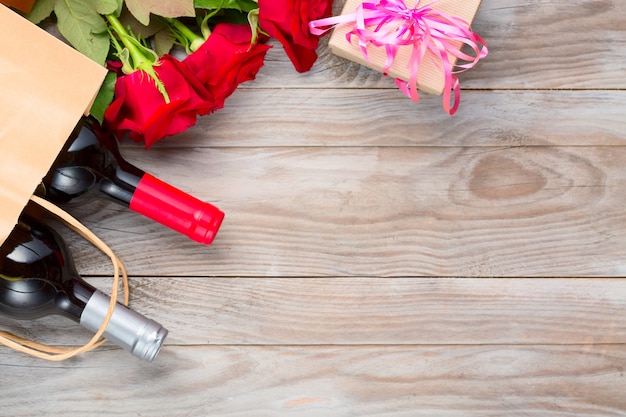 Botellas de vino y flores color de rosa en la mesa de madera