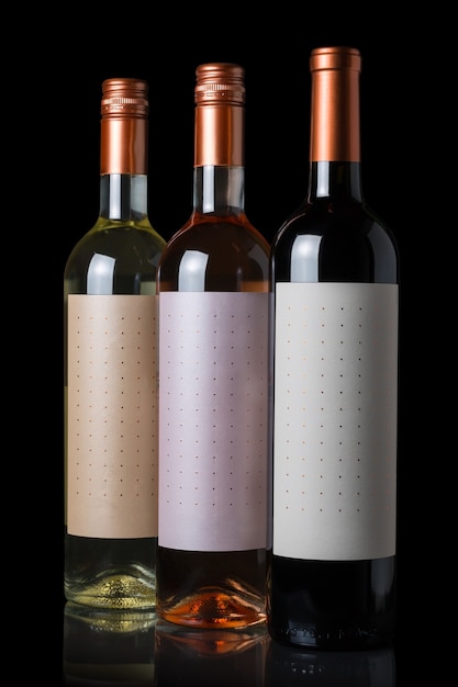 Botellas de vino tinto, blanco y rosado aislado en la pared negra.