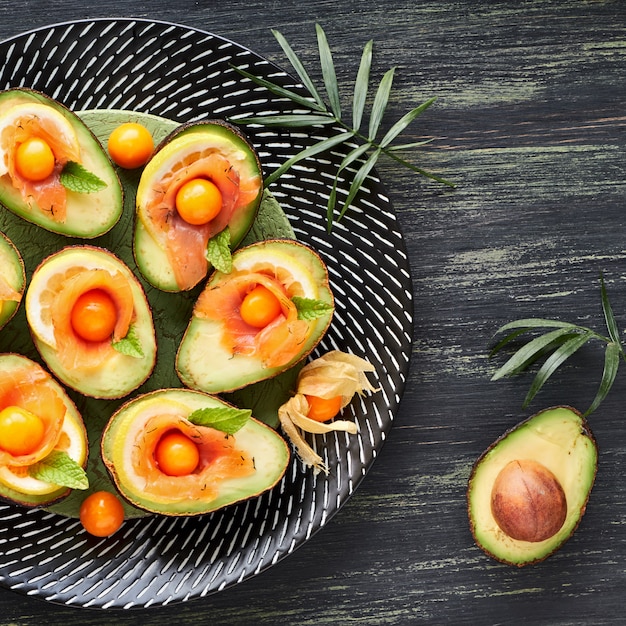 Botes de aguacate con salmón ahumado, limón, physalis y hojas de menta, vista superior