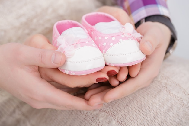 Botinhas de rosa para bebê recém-nascido nas mãos de mamãe e papai. gravidez