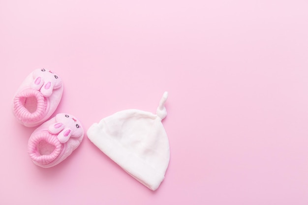 Botinhas em forma de lebres e um boné para um bebê em um fundo rosa com espaço de cópia