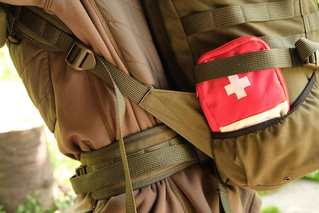 Un botiquín rojo de primeros auxilios con una cruz blanca en el bolsillo de una mochila verde militar táctica