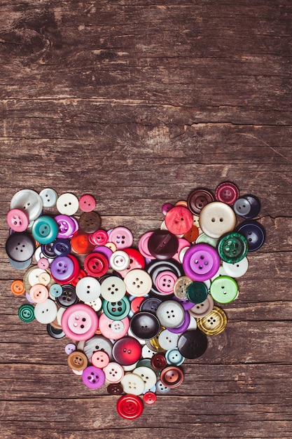 Botões coloridos em forma de coração na mesa de madeira vintage