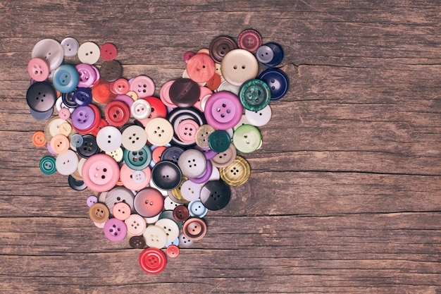 Botões coloridos em forma de coração na mesa de madeira vintage