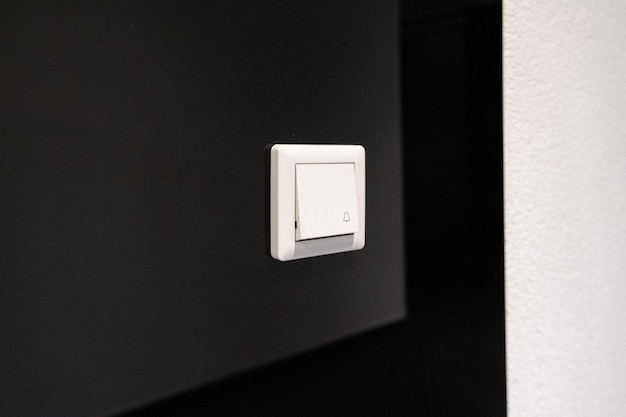 El botón blanco moderno del timbre de la puerta con un icono de campana en un wal oscuro