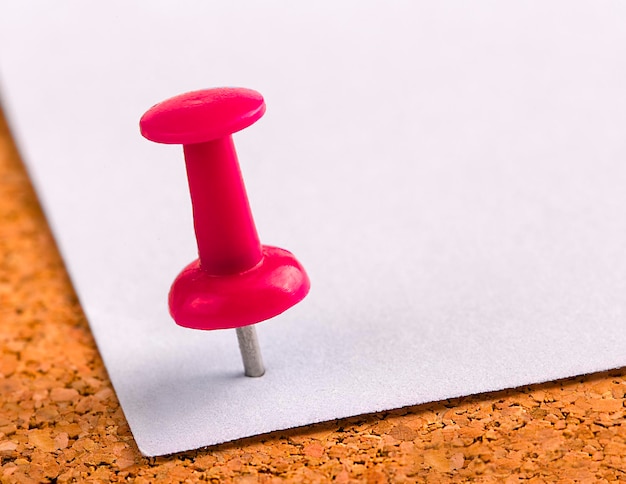 Foto el botón de plástico con una aguja clavada en una hoja de hierro de papel blanco sobre un tapón de madera