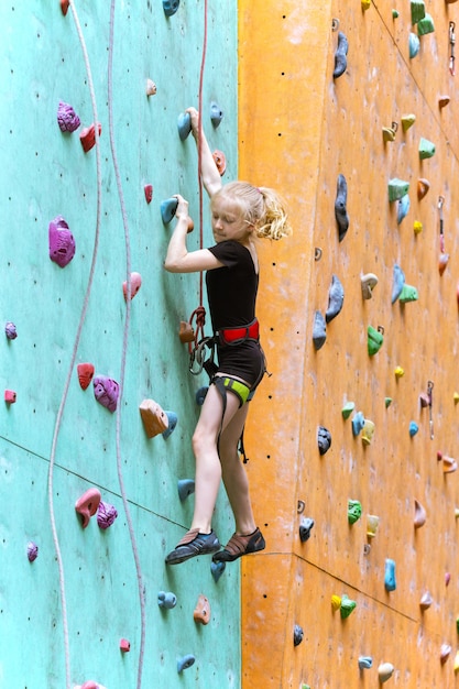 Bouldering, menina subindo a parede e pegas multicoloridas alpinista. Atividade de lazer