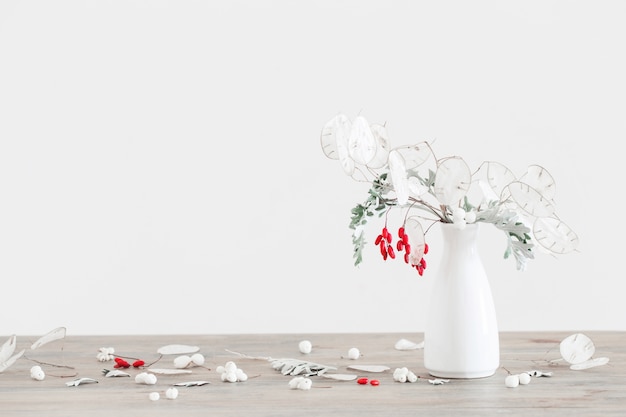 Bouquet com lunaria e frutas vermelhas em um vaso branco na mesa de madeira