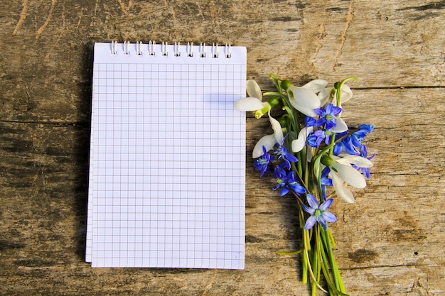 Bouquet de flores da primavera e o bloco de notas em branco sobre fundo de madeira rústico