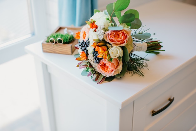 Bouquet de noiva de flores brancas e laranja em uma mesa branca.