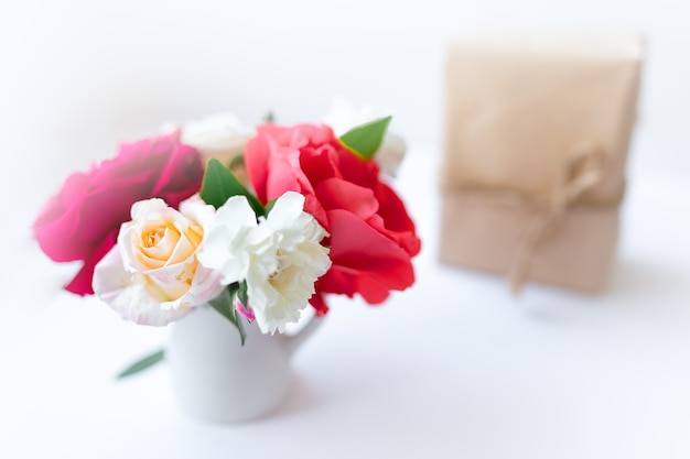 Bouquet de rosas com caixa de presente embrulhada em papel pardo ecológico presente no fundo branco, conceito de feriado romântico, espaço de cópia