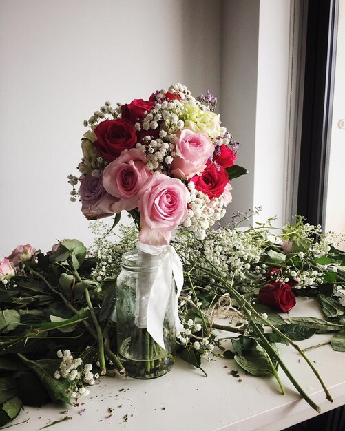 Foto bouquet de rosas em frasco por plantas na mesa