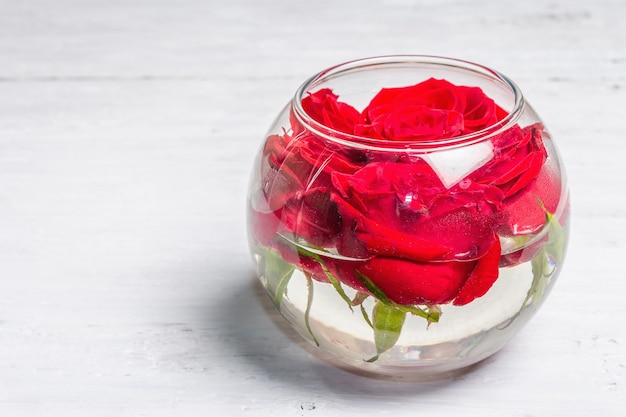 Bouquet de rosas vermelhas frescas em vaso de vidro. O conceito festivo para casamentos, aniversários, dia 8 de março, dia das mães ou dos namorados. Cartão de felicitações, placas de madeira brancas