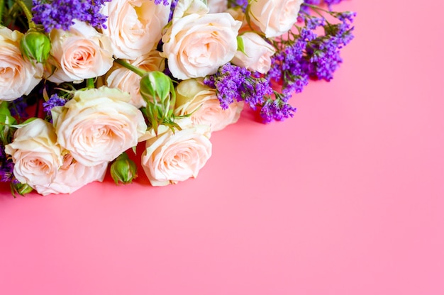 Bouquet von cremefarbenen Rosen und leuchtend lila Blumen in voller Blüte auf einem rosa Hintergrund mit Platz für Text.