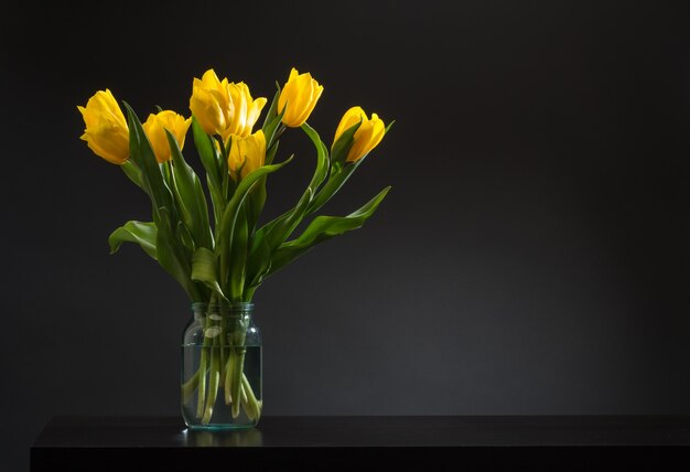 Bouquet von schönen frischen gelben Tulpen im Tau auf dunklem Hintergrund. Stilllebenfoto