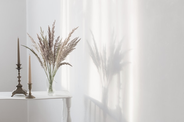 Bouquet wilde Blumen und Kerzen im Sonnenlicht im weißen Innenraum