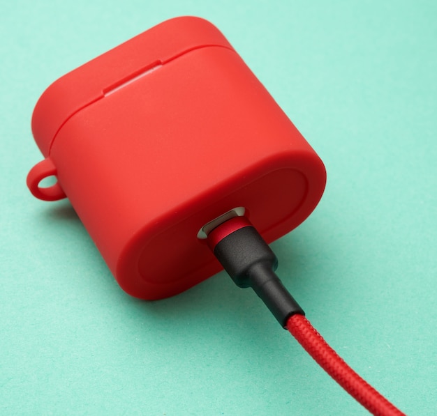 Box mit einem Kopfhörer-Ladegerät in einer roten Hülle am Kabel auf grünem Grund