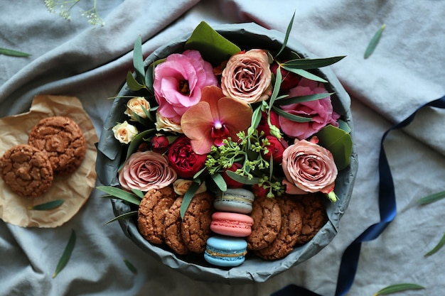 Box mit frischen Blumen und Makronen auf grauem Stoffhintergrund