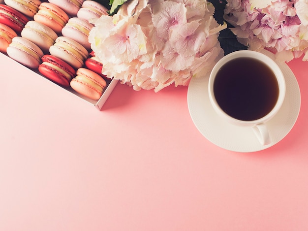 Box mit Makronen und Tasse Kaffee, Blumen auf rosa