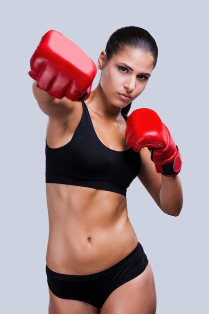 Boxe de mulher. Mulher jovem e bonita esportiva boxe em pé contra um fundo cinza