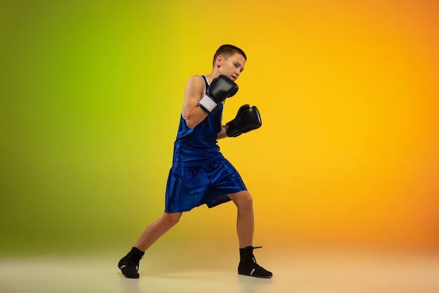 Boxeador adolescente contra el fondo del estudio de neón degradado en movimiento de patadas, boxeo