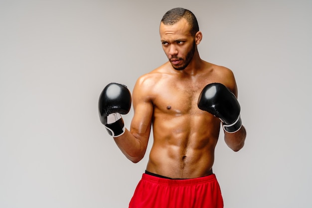 Boxeador africano joven confiado en guantes de boxeo que se colocan sobre la pared gris clara