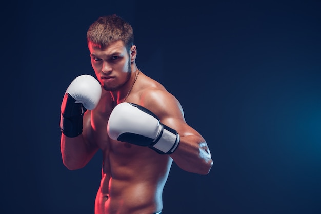 Boxeador sin camisa con guantes sobre fondo oscuro. Aislar