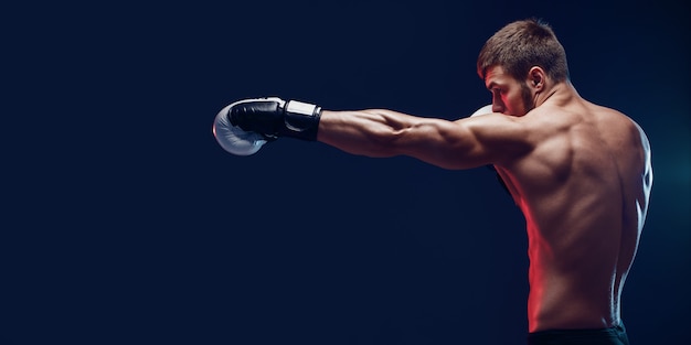 Boxeador sin camisa con guantes sobre fondo oscuro. Aislar