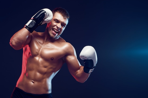 Boxeador sin camisa con guantes sobre fondo oscuro. Aislar