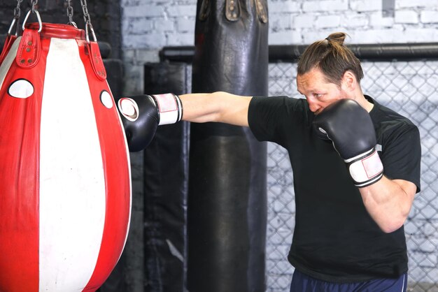 Boxeador fuerte está entrenando en un gimnasio peleando con saco de boxeo Entrenamiento de boxeo