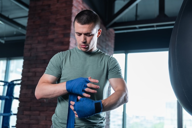 Boxeador en gimnasio. Boxeador hábil prometedor de pelo oscuro con muñequeras azules en un gimnasio moderno y ligero