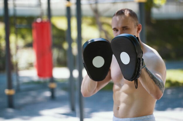 Boxeador de hombre musculoso en entrenamiento de patas de boxeo en el parque de verano