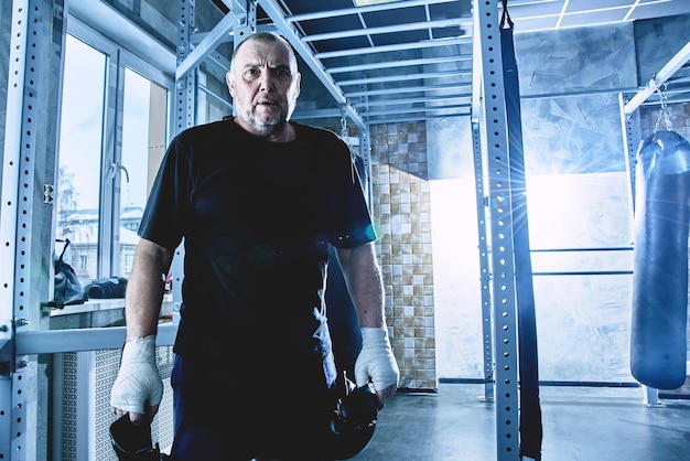 Boxeador masculino adulto de pelo gris en el entrenamiento en el boxeo de gimnasio con guantes El concepto de un estilo de vida saludable en la vejez