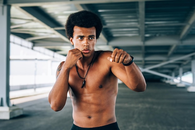 Boxeador masculino sin camisa haciendo ejercicio debajo del puente