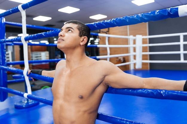 Boxeador masculino pensativo em pé na academia e olhando para cima